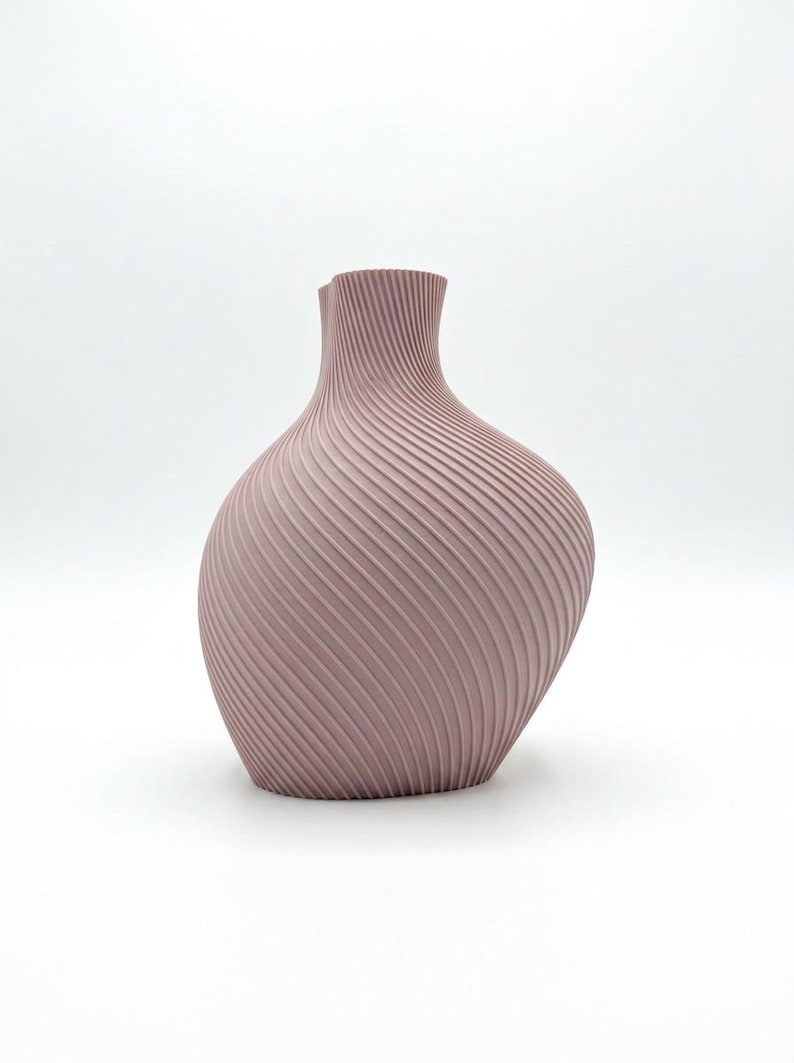 Puede incluir: Un jarr&oacute;n de color malva con un dise&ntilde;o texturizado &uacute;nico. El jarr&oacute;n tiene un cuerpo bulboso y un cuello delgado. La superficie presenta una serie de l&iacute;neas diagonales y estriadas que envuelven el jarr&oacute;n, creando un efecto de espiral. El jarr&oacute;n est&aacute; sobre un fondo blanco.