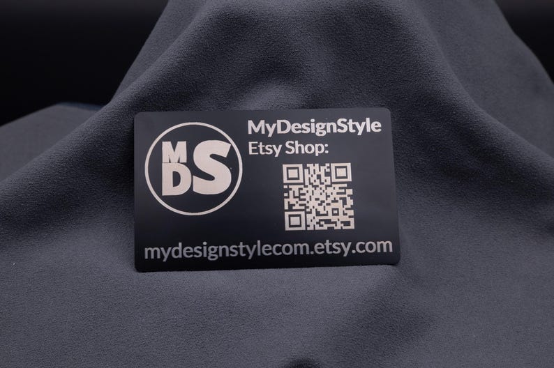Visitenkarte aus schwarzem Aluminium mit Gravur „MDS“ Logo, Etsy-Shop-URL und QR-Code. Die stabile Metallkarte ist modern, elegant und ideal für Branding, Marketing und als langlebige Businesskarte mit individueller Gravur.