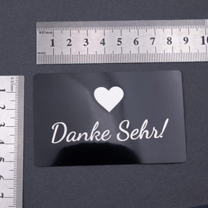 Schwarze Aluminiumkarte mit Gravur „Danke Sehr!“ und Herzsymbol, fotografiert mit Lineal zur Größenangabe. Format entspricht einer klassischen Kreditkarte (8,6 × 5,4 cm). Langlebig, robust und stilvoll – ideal als Dankeskarte oder personalisierte Visitenkarte für professionelle Businessauftritte.