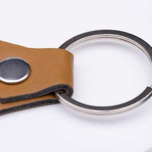 Detailaufnahme des silbernen Schlüsselrings eines personalisierten Schlüsselanhängers aus veganem Kunstleder. Der Fokus liegt auf der stabilen Metallniete und der sauberen Verarbeitung des hellbraunen Leders. Das Bild zeigt die Materialqualität und das präzise Handwerk dieses edlen Accessoires für Schlüssel oder Taschen.