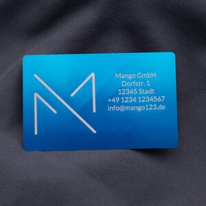 Businesskarte aus Aluminium in Blau mit Mango GmbH-Logo und Kontaktdaten: Adresse, Telefonnummer und E-Mail. Die matte Oberfläche und abgerundeten Kanten verleihen der Karte eine exklusive, professionelle Wirkung. Diese gravierte Metallkarte ist die ideale Alternative zu Papierkarten und unterstreicht modernes, stilvolles Firmenbranding bei Geschäftskontakten und Networking.