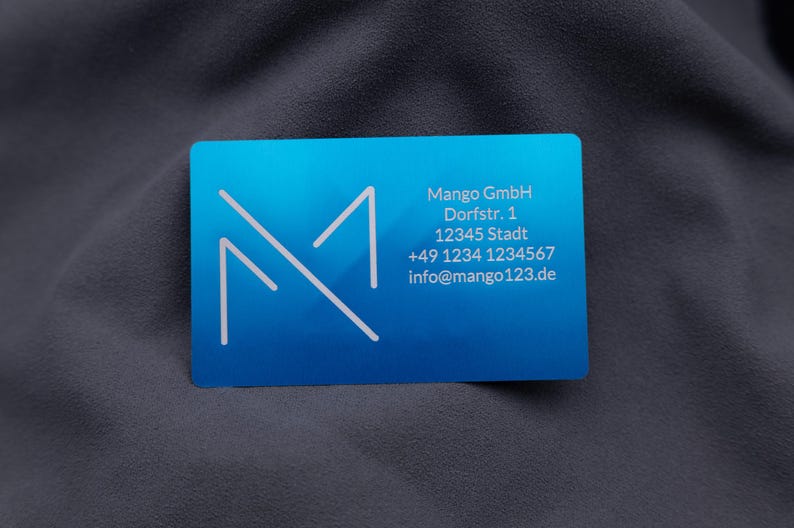 Businesskarte aus Aluminium in Blau mit Mango GmbH-Logo und Kontaktdaten: Adresse, Telefonnummer und E-Mail. Die matte Oberfläche und abgerundeten Kanten verleihen der Karte eine exklusive, professionelle Wirkung. Diese gravierte Metallkarte ist die ideale Alternative zu Papierkarten und unterstreicht modernes, stilvolles Firmenbranding bei Geschäftskontakten und Networking.