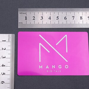 Aluminium-Visitenkarte in Metallic-Lila mit Mango Digital Logo, dargestellt neben einem Lineal zur Größenansicht. Standardgröße 85 x 54 mm, perfekt passend für Geldbeutel oder Visitenkartenetui. Die stabile Metalloberfläche ist kratzfest und langlebig, während das elegante Design für einen exklusiven Eindruck sorgt. Diese Karte vereint hochwertige Optik mit praktischer Funktionalität im Alltag.