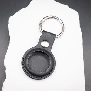 Rückansicht eines schwarzen AirTag Schlüsselanhängers aus PU Leder. Die runde AirTag Aufnahme ist hochwertig verarbeitet und sicher vernäht. Edelstahlring und Druckknopf bieten festen Halt. Dezentes funktionales Design für den täglichen Gebrauch und sichere Befestigung des Apple AirTag.