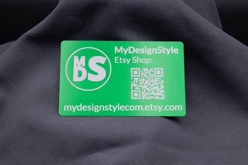 Grüne Aluminium-Visitenkarte mit dem Logo "MDS", einem QR-Code und Etsy-Shop-Link. Das klare weiße Gravurdesign auf der glänzenden Oberfläche sorgt für ein modernes und professionelles Erscheinungsbild. Die stabile Karte ist langlebig und praktisch, ideal zur Weitergabe an Kunden, die direkten Zugriff auf den Onlineshop erhalten und gleichzeitig ein exklusives Design in den Händen halten.
