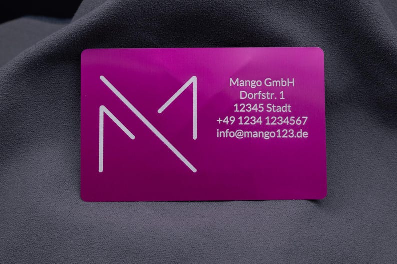 Lila Aluminium-Visitenkarte mit Mango GmbH Logo und detaillierten Geschäftsdaten: Adresse, Telefonnummer und E-Mail. Die lasergravierte Schrift hebt sich klar und dauerhaft von der metallischen Oberfläche ab. Diese hochwertige Geschäftskarte ist ideal für Networking, Kundenkontakte und Geschäftspartner. Dank der stabilen Aluminiumstruktur vermittelt sie Exklusivität und hebt sich deutlich von herkömmlichen Papierkarten ab.