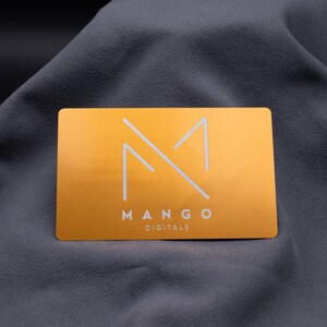 Elegante Aluminium-Visitenkarte in Hellgold mit modernem Mango-Digitals-Logo. Das minimalistische Design besticht durch klare Linien, matt gebürstete Oberfläche und eine exklusive Gravur. Mit Standard-Visitenkartengröße und abgerundeten Kanten wirkt sie edel und professionell. Ideal für Firmen, die Wert auf ein modernes, langlebiges und auffälliges Branding legen und mit einer besonderen Metallkarte überzeugen möchten.