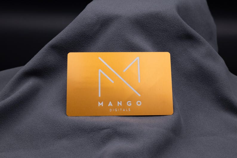 Elegante Aluminium-Visitenkarte in Hellgold mit modernem Mango-Digitals-Logo. Das minimalistische Design besticht durch klare Linien, matt gebürstete Oberfläche und eine exklusive Gravur. Mit Standard-Visitenkartengröße und abgerundeten Kanten wirkt sie edel und professionell. Ideal für Firmen, die Wert auf ein modernes, langlebiges und auffälliges Branding legen und mit einer besonderen Metallkarte überzeugen möchten.