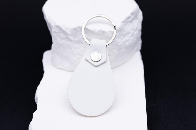 Rückseite des weißen Schlüsselanhängers aus hochwertigem veganem Kunstleder mit silbernem Druckknopf und stabilem Metallring. Die glatte Oberfläche und saubere Verarbeitung verleihen dem Anhänger eine edle Optik. Perfekt als minimalistisches Accessoire oder Geschenkidee mit individueller Gravur. Das vegane Leder bietet eine tierfreundliche, langlebige Alternative zu Echtleder.