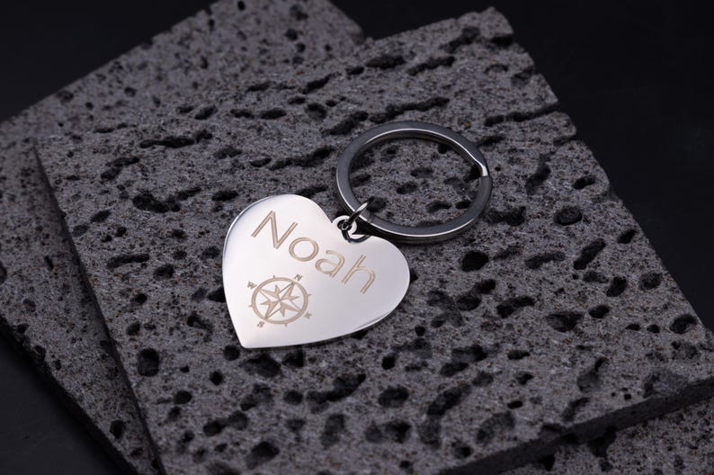 Nahaufnahme des gravierten Herz-Schlüsselanhängers mit Kompassmotiv. Der Name „Noah“ ist präzise per Laser eingraviert, die Oberfläche spiegelt leicht und zeigt die hochwertige Verarbeitung. Der Schlüsselring ist robust und sicher befestigt. Ideal als stilvolles, personalisiertes Geschenk aus rostfreiem Edelstahl.