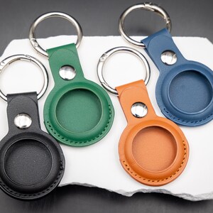 Rückseite von vier AirTag Schlüsselanhängern aus hochwertigem PU Leder in verschiedenen Farben. Die runde Aufnahme für den Apple AirTag ist sauber eingefasst und vernäht. Sichtbar sind die feine Lederstruktur sowie stabile Edelstahldrückknöpfe und Schlüsselringe. Praktisches Zubehör zum sicheren Befestigen von AirTags an Schlüsselbund Tasche oder Rucksack.