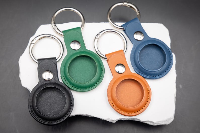 Rückseite von vier AirTag Schlüsselanhängern aus hochwertigem PU Leder in verschiedenen Farben. Die runde Aufnahme für den Apple AirTag ist sauber eingefasst und vernäht. Sichtbar sind die feine Lederstruktur sowie stabile Edelstahldrückknöpfe und Schlüsselringe. Praktisches Zubehör zum sicheren Befestigen von AirTags an Schlüsselbund Tasche oder Rucksack.