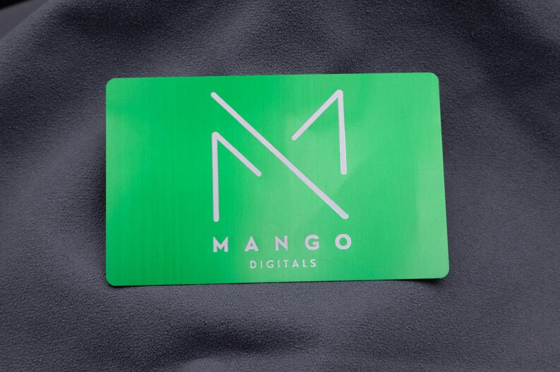 Eine einzelne grüne Visitenkarte aus Aluminium mit lasergraviertem Logo "MANGO DIGITALS". Das minimalistische Design in Weiß kontrastiert mit der metallisch glänzenden Oberfläche. Die hochwertige Gravur verleiht der Karte ein elegantes Erscheinungsbild, ideal für moderne Marken und kreative Unternehmer, die Wert auf edles, langlebiges Design legen und einen bleibenden Eindruck hinterlassen möchten.