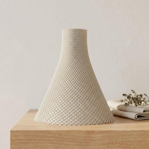 Peut inclure: Un vase conique cr&egrave;me avec un ext&eacute;rieur &agrave; motif de losanges. Le vase repose sur une surface en bois de couleur claire. Le vase a une base large qui se r&eacute;tr&eacute;cit en un col plus &eacute;troit. D&eacute;coration int&eacute;rieure.