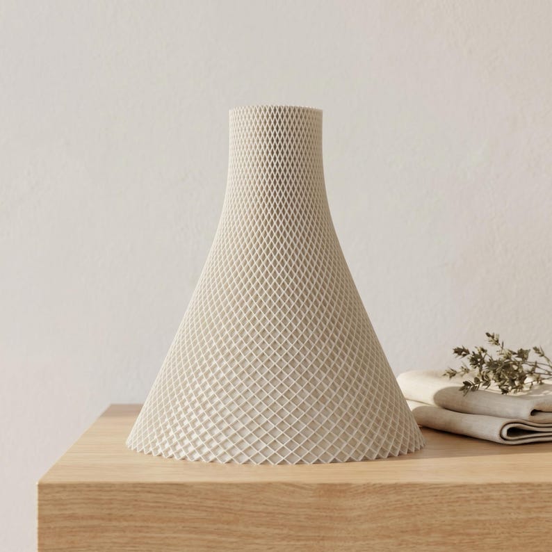 Peut inclure: Un vase conique cr&egrave;me avec un ext&eacute;rieur &agrave; motif de losanges. Le vase repose sur une surface en bois de couleur claire. Le vase a une base large qui se r&eacute;tr&eacute;cit en un col plus &eacute;troit. D&eacute;coration int&eacute;rieure.