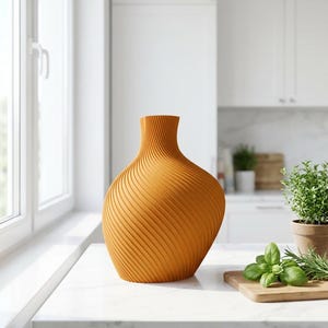 Puede incluir: Un jarr&oacute;n naranja con un dise&ntilde;o texturizado y arremolinado. El jarr&oacute;n tiene una base ancha que se estrecha hacia un cuello estrecho. El jarr&oacute;n est&aacute; sobre una encimera blanca en un entorno de cocina. La cocina tiene gabinetes blancos y una ventana.