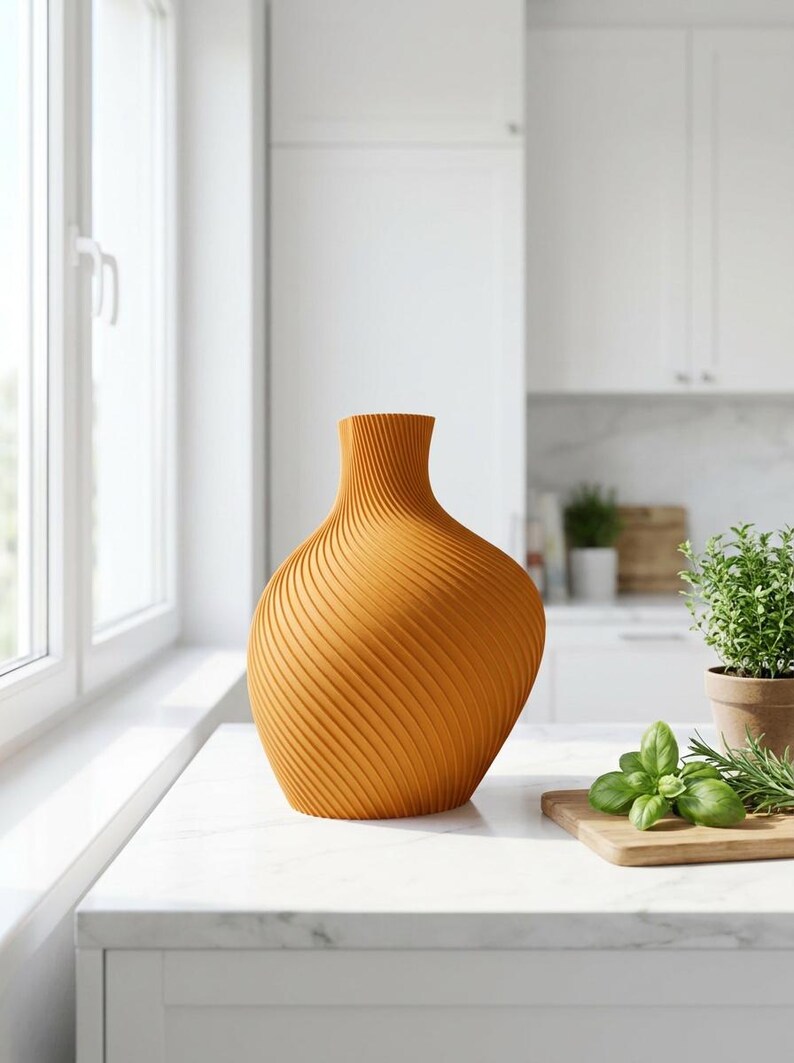 Puede incluir: Un jarr&oacute;n naranja con un dise&ntilde;o texturizado y arremolinado. El jarr&oacute;n tiene una base ancha que se estrecha hacia un cuello estrecho. El jarr&oacute;n est&aacute; sobre una encimera blanca en un entorno de cocina. La cocina tiene gabinetes blancos y una ventana.