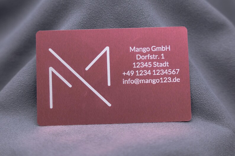 Visitenkarte aus roségoldenem Aluminium mit Gravur von Mango-Logo, Adresse, Telefonnummer und E-Mail. Die matte Oberfläche wirkt hochwertig, die Karte ist robust und langlebig. Perfekt für Unternehmer, die eine moderne, exklusive Businesskarte für Networking und professionelle Präsentationen nutzen möchten.