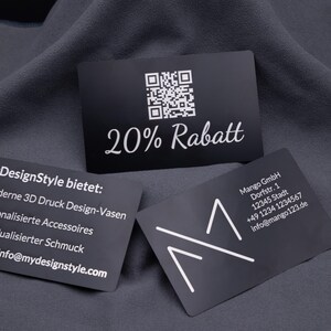 Schwarze Visitenkarte aus Aluminium mit Gravur „20% Rabatt“ und QR-Code, daneben weitere gravierte Karten mit Firmenlogo und Angeboten. Die stabile Metallkarte ist eine elegante Alternative zu Papierkarten, ideal für Gutscheine, Rabattaktionen oder als auffälliges Werbemittel im Business-Alltag.