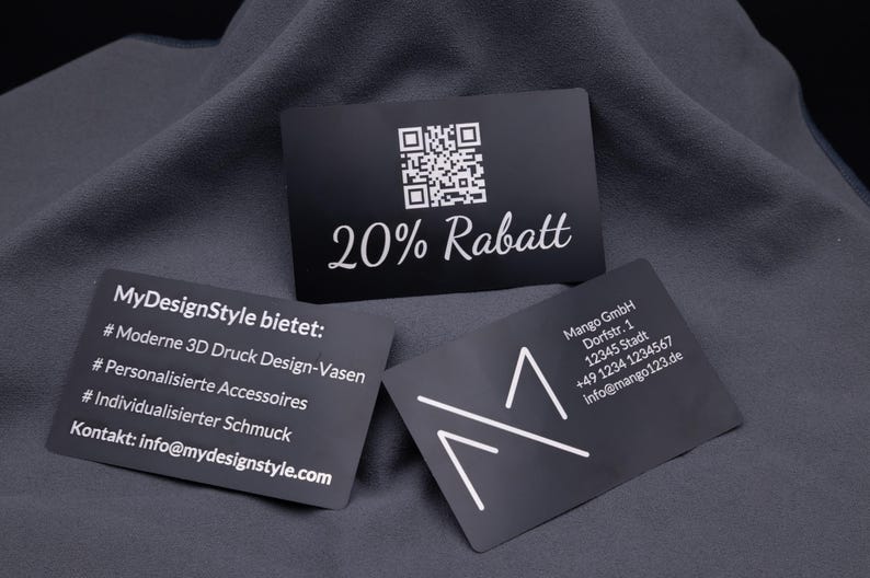 Schwarze Visitenkarte aus Aluminium mit Gravur „20% Rabatt“ und QR-Code, daneben weitere gravierte Karten mit Firmenlogo und Angeboten. Die stabile Metallkarte ist eine elegante Alternative zu Papierkarten, ideal für Gutscheine, Rabattaktionen oder als auffälliges Werbemittel im Business-Alltag.