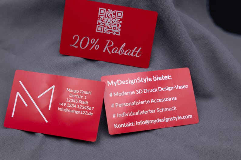 Drei rote Aluminiumkarten mit Gravur. Oben eine Rabattkarte mit QR-Code und Gravur „20% Rabatt“, unten links eine Businesskarte mit Mango-Logo und Kontaktdaten, daneben eine Karte mit Produktübersicht: 3D-Druck-Designvasen, personalisierte Accessoires, individueller Schmuck. Die edlen Metallkarten sind robust, langlebig und ein stilvolles Marketing- und Businessinstrument.