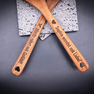 Kochlöffelset aus Akazienholz mit Gravur, bestehend aus einem Pfannenwender und einem Löffel. Beide sind personalisiert mit Namen und Spruch. Das natürliche Holz, die feine Gravur und das Herzloch im Griff machen das Set zu einem beliebten, praktischen Geschenk für Paare und Küchenliebhaber.