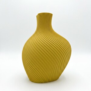 Puede incluir: Jarr&oacute;n amarillo mostaza con un dise&ntilde;o espiral texturizado &uacute;nico. El jarr&oacute;n tiene una base ancha que se estrecha hacia un cuello estrecho. El jarr&oacute;n mide aproximadamente 25 cm de alto y es un adorno decorativo.