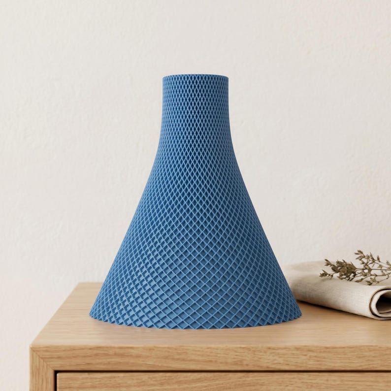 Peut inclure: Un vase d&eacute;coratif bleu avec une surface textur&eacute;e &agrave; motifs de losanges. Le vase a une forme conique &eacute;vas&eacute;e et repose sur une surface en bois. Le vase est de couleur bleu uni et a une base large.