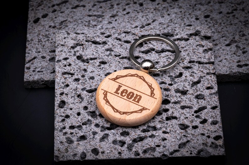Runder Schlüsselanhänger aus Holz mit Gravur „Leon“. Das Motiv zeigt einen dekorativen Rahmen im rustikalen Stil, mittig der Name. Holzanhänger mit Metallring – natürlich, stabil und personalisierbar.