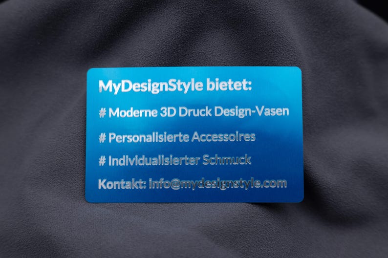 Blaue Aluminiumkarte mit Gravur der Angebote von MyDesignStyle: moderne 3D-Druck Vasen, personalisierte Accessoires und individueller Schmuck. Ergänzt mit Kontakt-E-Mail eignet sich die Karte perfekt als Werbemittel oder Beileger. Die hochwertige Metallausführung sorgt für Eleganz, Langlebigkeit und einen besonderen Eindruck – ideal für kreative Unternehmer und Designer.