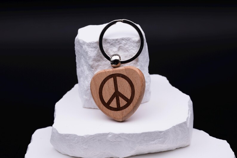 Herz Schlüsselanhänger aus Holz mit eingraviertem Peace-Symbol. Die feine Gravur verleiht dem Anhänger eine zeitlose und moderne Optik. Personalisierbar mit weiteren Namen oder Symbolen eignet er sich als Geschenk für Freunde, Paare oder Kinder. Ein nachhaltiges Accessoire, das durch schlichte Eleganz und Individualität überzeugt und sowohl im Alltag als auch als besonderes Geschenk Freude bereitet.