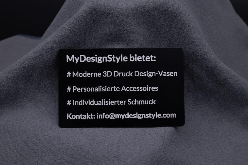 Schwarze Metall-Visitenkarte mit Gravur von Produkten und Leistungen: moderne 3D-Druck-Vasen, personalisierte Accessoires, individueller Schmuck. Diese Karte ist eine stilvolle Präsentation der eigenen Services und eine langlebige Alternative zu Papierkarten.