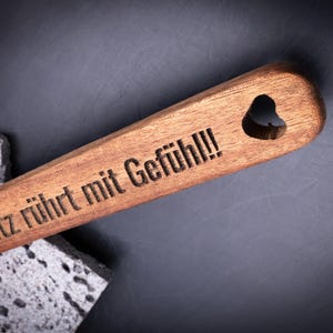 Detailaufnahme des gravierten Holzlöffels aus Akazienholz mit der Gravur „Moritz rührt mit Gefühl!!!“ und kleinem Symbol. Das Herzloch im Griff sorgt für dekorative Aufhängemöglichkeit. Die feine Lasergravur ist dauerhaft eingebrannt – ideal für personalisierte Geschenke zum Kochen, Braten oder Backen.