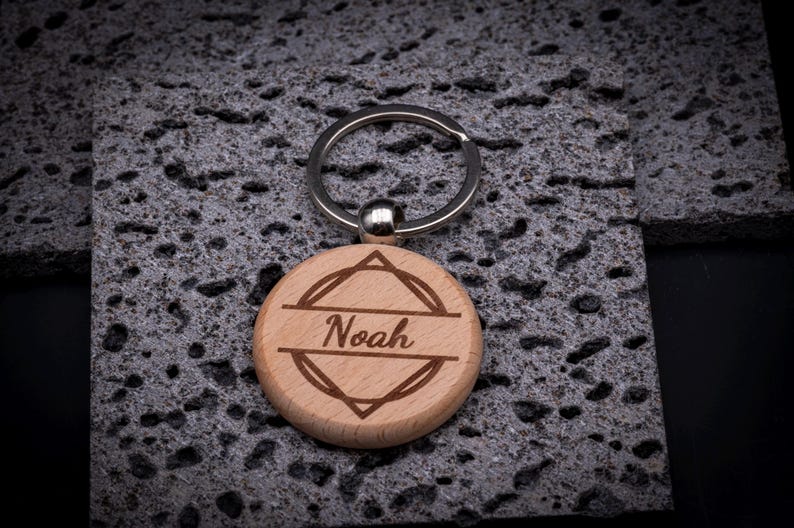 Runder Schlüsselanhänger aus Holz mit Gravur „Noah“. Moderner geometrischer Rahmen mit klaren Linien. Robuster Anhänger mit Metallring, perfekt als personalisierter Begleiter.