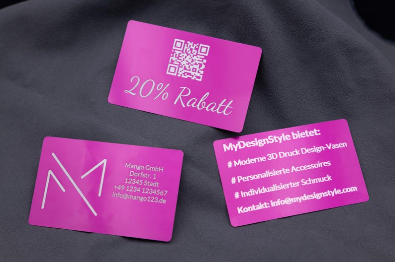 Hochwertige Aluminium-Visitenkarten in Lila mit unterschiedlichen Gravuren: eine Karte zeigt „20 % Rabatt“ mit QR-Code, eine enthält die Firmenadresse der Mango GmbH, und eine dritte listet MyDesignStyle-Angebote wie 3D Druck Design-Vasen und personalisierte Accessoires. Jede Karte überzeugt durch kratzfeste Gravur, langlebiges Material und edle Metallic-Optik, perfekt für Unternehmen und kreatives Marketing.