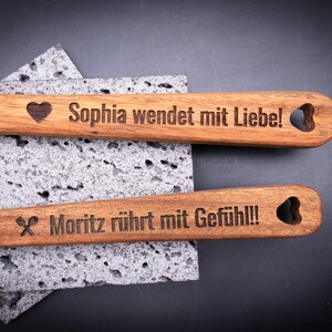 Zwei gravierte Kochlöffel aus Akazienholz mit den Gravuren „Sophia wendet mit Liebe!“ und „Moritz rührt mit Gefühl!!!“. Beide Griffe sind mit Herz-Ausschnitt und Symbolen versehen. Die präzise Lasergravur hebt sich kontrastreich vom warmen Holzton ab. Perfektes personalisierbares Geschenk für Hobbyköche, Paare oder Freunde, die gerne gemeinsam kochen.