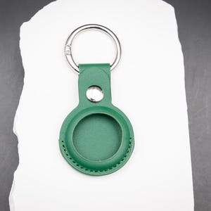 Rückansicht eines grünen AirTag Schlüsselanhängers aus PU Leder. Die runde Einfassung für den Apple AirTag ist glatt verarbeitet und fest vernäht. Der Edelstahl Druckknopf sorgt für sicheren Halt des AirTags. Hochwertiges und langlebiges Zubehör für den Alltag, passend für Schlüssel Taschen oder Gepäck.