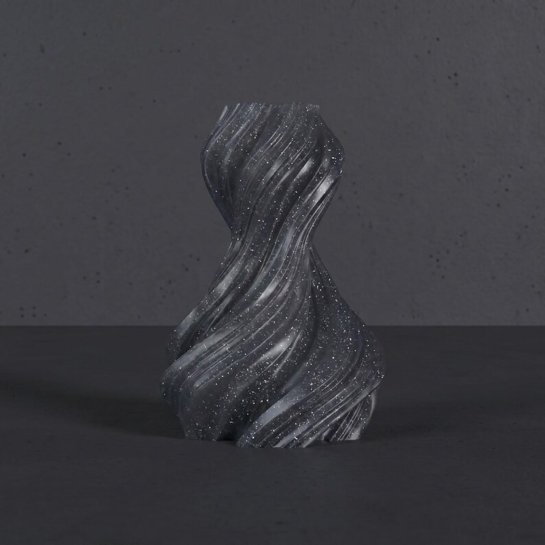 K&ouml;nnte beinhalten: Eine dunkelgraue, wirbelnde Vase mit einer strukturierten, glitzernden Oberfl&auml;che. Die Vase hat ein einzigartiges, gedrehtes Design und steht auf einer dunklen Oberfl&auml;che. Die Gesamt&auml;sthetik ist modern und k&uuml;nstlerisch.