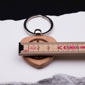 Herz Schlüsselanhänger aus Holz mit Peace-Symbol und Maßband zur Darstellung der Größe. Personalisierbar mit individuellen Gravuren wie Namen oder Symbolen, ist dieser Anhänger ein besonderes Geschenk für Familie, Freunde oder Partner. Hergestellt aus hochwertigem Naturholz, modern graviert und langlebig. Perfekt als Geschenkidee für Geburtstag, Jubiläum, Hochzeitstag oder für den Alltag.