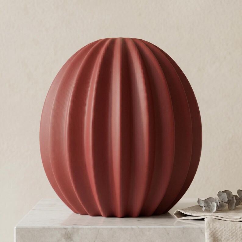 May include: A terracotta-coloured, spherical vase with vertical, ribbed detailing. The vase has a rounded shape and sits on a marble surface. The design is simple and modern, suitable for home decor.