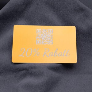 Exklusive Rabattkarte aus Aluminium in Hellgold mit Gravur „20% Rabatt“ und integriertem QR-Code. Mit abgerundeten Kanten, matter Oberfläche und edler Gravur eignet sich die Karte hervorragend als langlebiges Marketingtool für Shops, Events und Kundenaktionen. Ein stilvolles Werbemittel, das mit seinem eleganten Metall-Design Professionalität und Qualität unterstreicht.