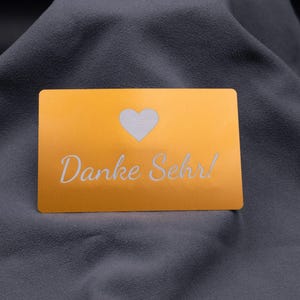 Hellgoldene Aluminium-Visitenkarte mit Gravur-Logo von Mango GmbH. Links ein modernes M-Symbol, rechts Kontaktdaten mit Adresse, Telefonnummer und Mail. Die klare, elegante Gestaltung mit matter Oberfläche und abgerundeten Kanten macht die Karte zu einer exklusiven Alternative zur klassischen Papierkarte. Perfekt für Business-Kontakte, Networking und als auffällige Premium-Firmenkarte.