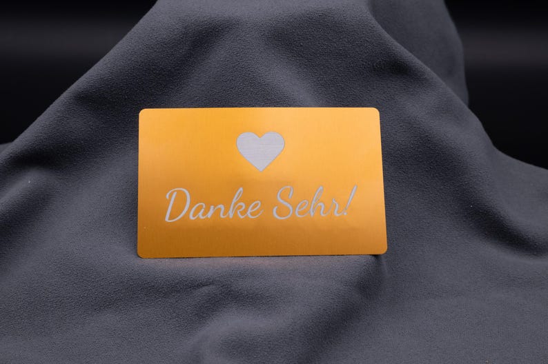 Hellgoldene Aluminium-Visitenkarte mit Gravur-Logo von Mango GmbH. Links ein modernes M-Symbol, rechts Kontaktdaten mit Adresse, Telefonnummer und Mail. Die klare, elegante Gestaltung mit matter Oberfläche und abgerundeten Kanten macht die Karte zu einer exklusiven Alternative zur klassischen Papierkarte. Perfekt für Business-Kontakte, Networking und als auffällige Premium-Firmenkarte.