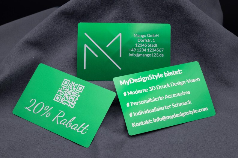 Drei grüne Aluminium-Visitenkarten mit lasergravierten Details. Eine Karte zeigt die Aufschrift "20% Rabatt" mit QR-Code, eine Firmenadresse mit Logo, die dritte eine Angebotsübersicht zu 3D-Designvasen und Schmuck. Die edle Metallic-Oberfläche macht die Karten zu einer langlebigen und auffälligen Wahl, perfekt für Unternehmen, die Wert auf Individualität und modernes Branding legen.