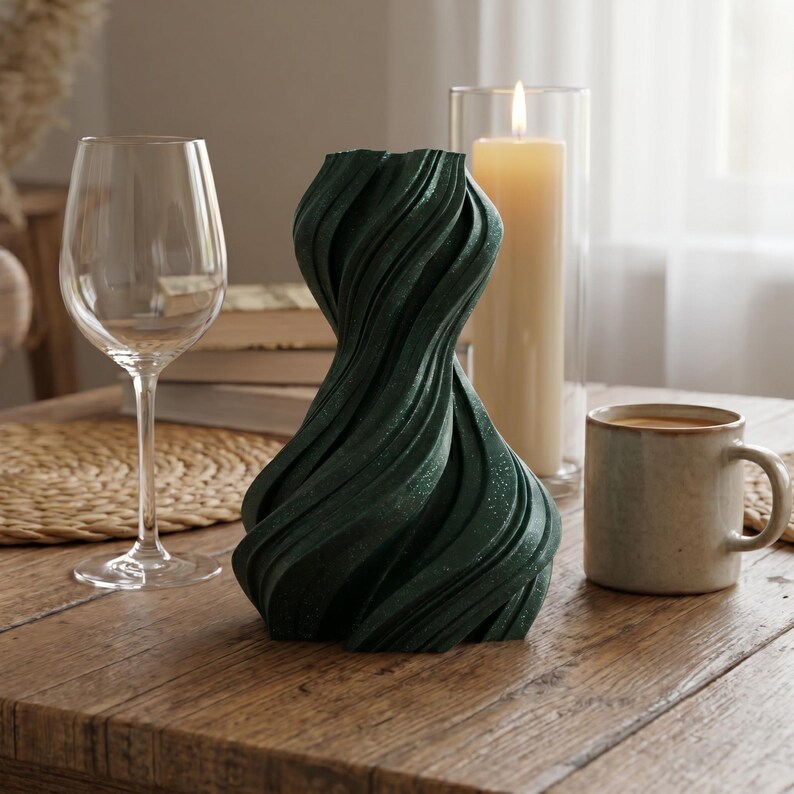 K&ouml;nnte beinhalten: Eine dunkelgr&uuml;ne Vase mit strukturiertem, wirbelndem Design. Ein Weinglas, eine brennende Kerze in einem Glasbeh&auml;lter und eine Kaffeetasse stehen auf einem Holztisch. Die Vase hat eine einzigartige, k&uuml;nstlerische Form.