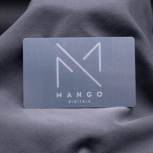 Visitenkarte aus Metall in Silber mit modernem Logo „Mango Digitals“. Die Aluminiumkarte überzeugt durch ihre matte Oberfläche, exklusive Haptik und langlebige Qualität. Eine stilvolle Alternative zur klassischen Papier-Visitenkarte, ideal für Unternehmer, Designer und Start-ups, die ihre Marke professionell und kreativ präsentieren möchten. Perfekt für Business-Events, Networking und Kundenbindung.