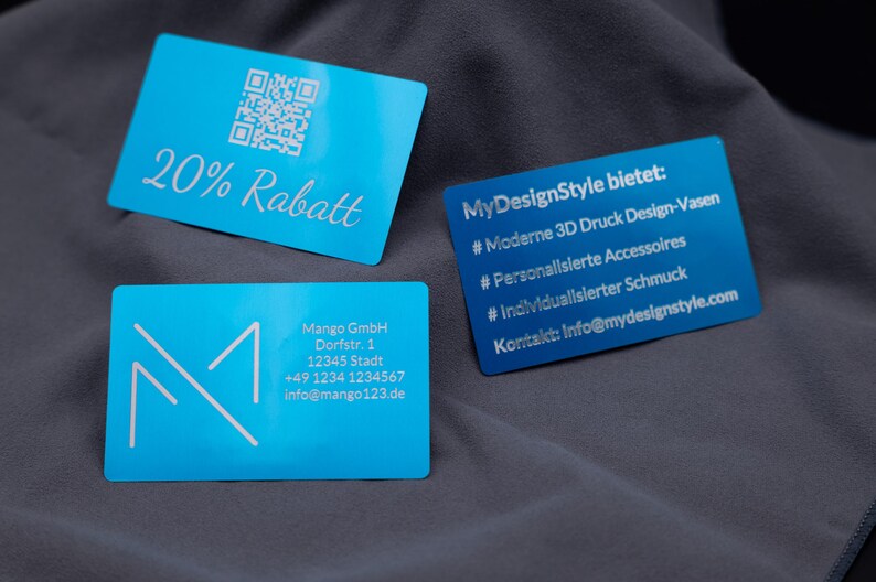 Varianten blauer Aluminiumkarten: eine Rabattkarte mit Gravur „20% Rabatt“ und QR-Code, eine MyDesignStyle-Karte mit Leistungsübersicht (3D-Druck Vasen, Accessoires, Schmuck), eine Firmenkarte von Mango GmbH mit Kontaktdaten und eine Mango-Logo-Karte. Diese robusten Metallkarten kombinieren edles Design mit Funktionalität und sind langlebige Alternativen zu klassischen Papierkarten.