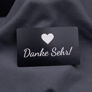 Einzelne schwarze Metallkarte im Kreditkartenformat mit eingraviertem Herzsymbol und Schriftzug „Danke Sehr!“. Die matte Aluminiumoberfläche wirkt edel und modern, perfekt als personalisierte Dankeskarte für Kunden, Geschäftspartner oder besondere Events.