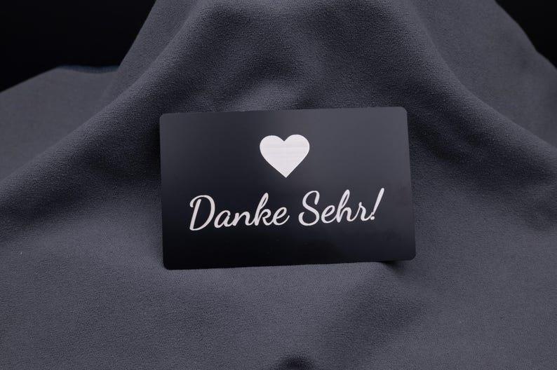Einzelne schwarze Metallkarte im Kreditkartenformat mit eingraviertem Herzsymbol und Schriftzug „Danke Sehr!“. Die matte Aluminiumoberfläche wirkt edel und modern, perfekt als personalisierte Dankeskarte für Kunden, Geschäftspartner oder besondere Events.