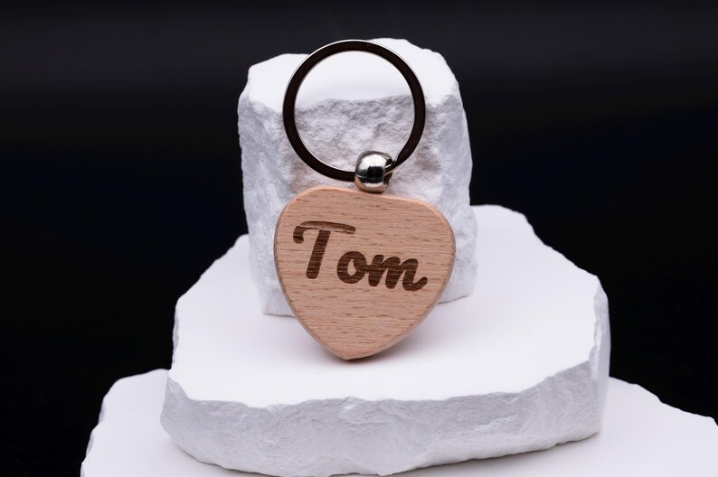 Gravierte Herz Schlüsselanhänger aus Holz mit dem Namen Tom in dekorativer Schrift. Der Anhänger kann individuell personalisiert werden und ist ideal als Geschenkidee für Partner, Freunde oder Kinder. Durch das schlichte, aber moderne Design mit Naturholz und Gravur ist er langlebig und praktisch für den Alltag. Perfekt geeignet für Geburtstage, Jubiläen oder als kleine Aufmerksamkeit.
